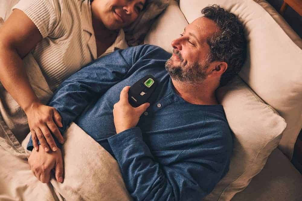 A couple lying in bed and smiling while the man holds an Inspire machine